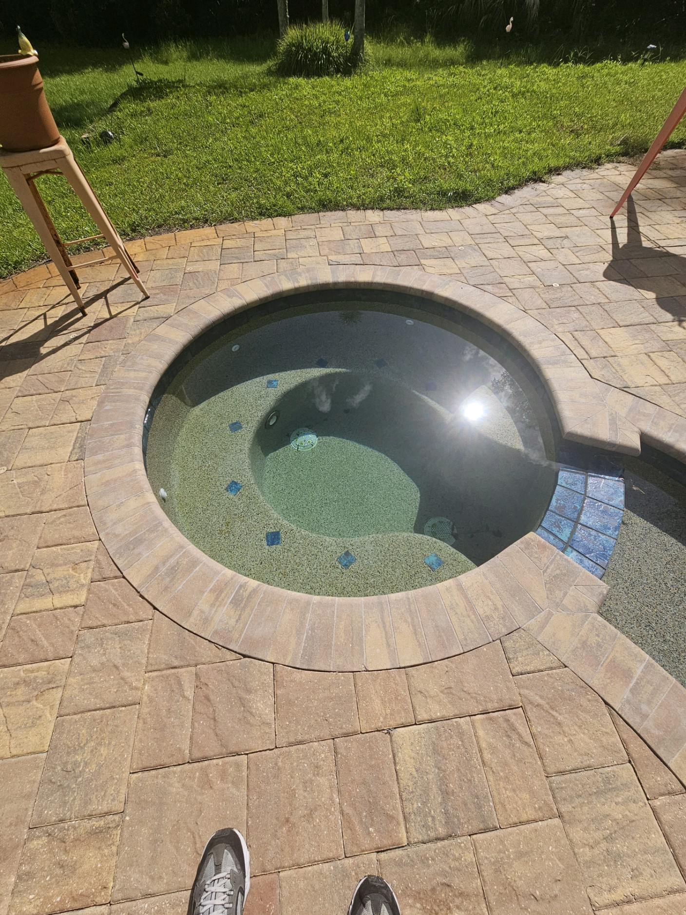 Clean circular spa with clear blue-green water on a brick paver surround