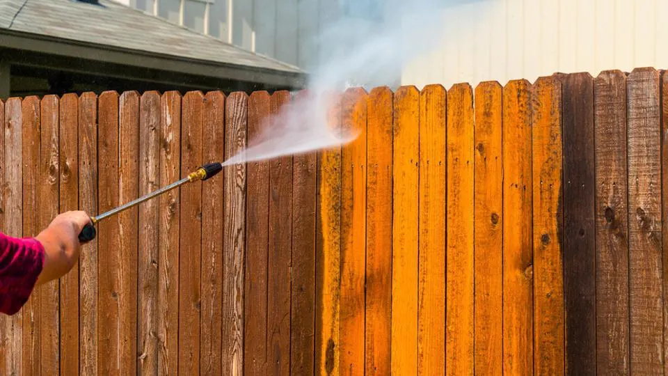 Pressure washing a wooden fence, showing the dramatic before and after cleaning result